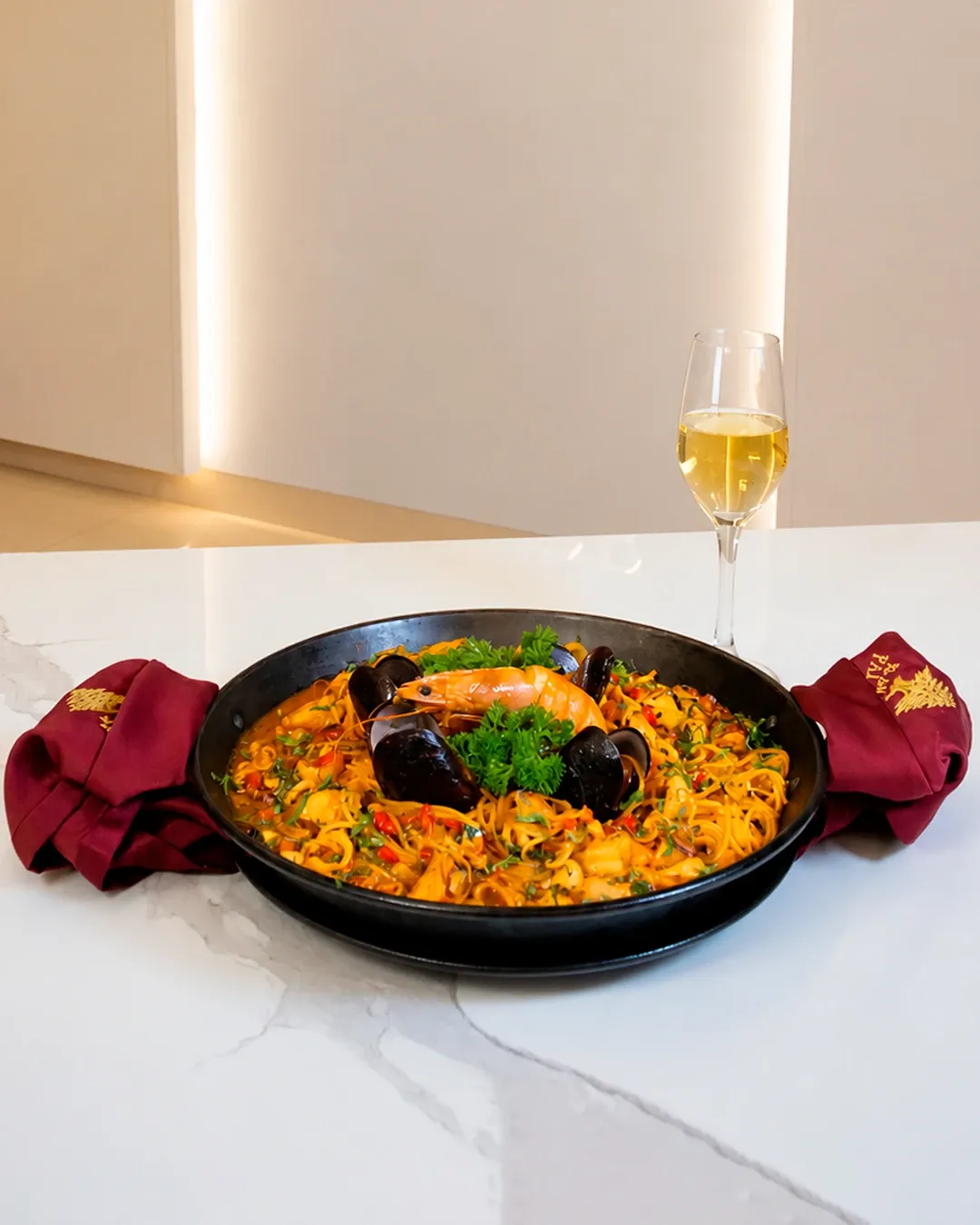 Fideuá de mariscos en paellera con una copa de vino, al centro de la mesa